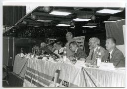 Personen sitzen an einem Tisch, ein Mann spricht in ein Mikrofon, 63. Delegiertenversammlung vom 25. Mai 1991, Hotel Nova-Park, Zürich