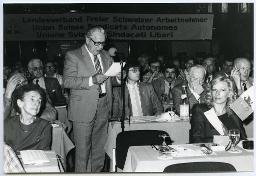 Mann spricht zum Publikum, welches hintereinander an Tischen sitzt; 60. Delegiertenversammlung 11. Mai 1985, Hotel Nova-Park Zürich