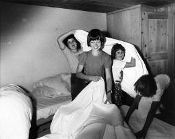 Vier Mädchen im Schlafzimmer machen die Betten und spielen mit einem Leintuch