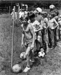 Knaben stehen im Gänsemarsch auf der Wiese, jeder von ihnen mit einem Fussball, Sonvico 1978