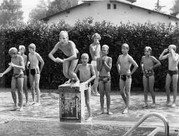 Knaben stehen im Gänsemarsch und warten vor dem Sprungbrett (Schwimmbad),  Magliaso 1978