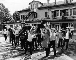 Kinder und Jungen winken vor dem Ferienhauskolonie Schwäbrig - Zwei Mädchen tragen zwei Teddybären (Plüschtiere), 1975