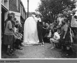 Der Schneemann - Frau das Gesicht des aus Stoff gebastelten Schneemannes malend und zusehende Kinder