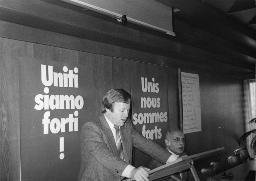Werner Rupff, Zentralsekretär Gewerkschaft Bau und Industrie (GBI), am Rednerpult stehend; im Hintergrund Plakate "Uniti sioamo forti!" - "Unis nous sommes forts!"; 02.02.1980