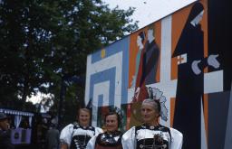SAFFA 1958: "Mathilda Paravicini, gestorben 1954; verwundete Mann und Frau zusammen in die Zukunft" - drei Frauen in Trachten; im Hintergrund grosse Stellwand mit Darstellung von Mathilda Paravicini; Zürich
