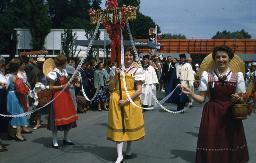 SAFFA 1958: "Maibaum" - Frau in Tracht einen Maibaum tragend; weitere Frauen stehen um Maibaum herum und halten Spitzenband; Zürich