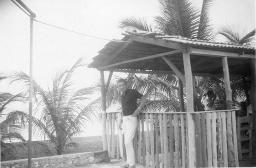 Bob Steffen steht an Strandbar; im Hintergrund Palmen und Meer, 1961