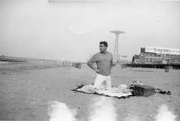 Bob Steffen am Strand mit Korb und Picknickdecke; im Hintergrund das Pier, 1961