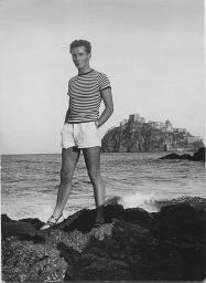 Bob Steffen auf Felsen am Meer stehend; im Hintergrund ein Dorf, um 1950