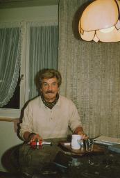 Bob Steffen mit Schnauz, Föhnwelle; an Tisch in bürgerlichem Ambiente, um 1980
