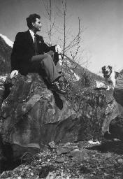 Bob Steffen in Anzug und Kravatte sitzt auf Stein, Gesicht im Profil; Hund auf anderem Stein, Gebirgslandschaft, um 1945