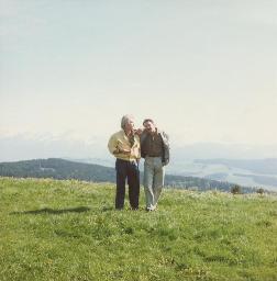 Bob Steffen (links) und Gerard Kuiper umarmen sich, sie stehen auf Wiese vor Alpenpanorama in der Ferne, 1989
