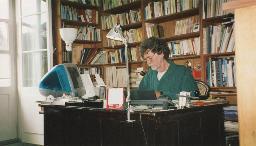 Giorgio Staro mit grünem Hemd und Pfeife sitzt an Bürotisch vor einer Bücherwand, 1998