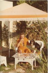 Bob Steffen im orangefarbenen Bademantel, Schnauz, melierte Locken, sitzt neben Hund auf Peddigrohr-Stuhl und trinkt aus Glas, 1980