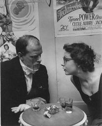 Peter F. Althaus als Erich von Strohheim und Eva Ebinger sitzend im Gespräch; Filmplakate, Kostümparty, 1958