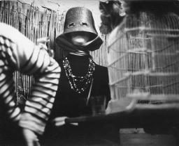 Meret Oppenheim mit Topfmaske und Augenschlitzen; sitzend, Arm von Ricco Wassmer, 1960