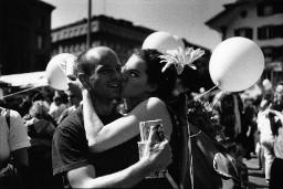 Frau mit Blume im Haar und weissem Luftballon am Rucksack, einen Mann auf die Wange küssend; Christopher Street Day 1998 in Bern