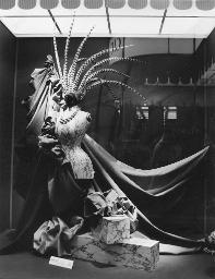 Stoffdrapierungen im Schaufenster von «Ciolina», Schaufensterpuppe mit Halskette und langen Federn auf dem Kopf