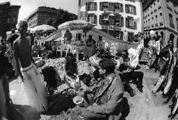 Zelt mit Sonnenschirm davor, auf dem Bundesplatz, im Vordergrund ein Mann mit nacktem Oberkörper und Rock aus weissen Fäden; Christopher Street Day 1998 in Bern