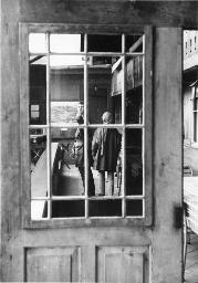 Foto mit Blick durch Fenster auf Holzlaube, im Hintergrund Bob Steffen und unbekannte Person von hinten, um 1970