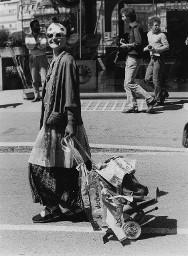 Verkleidete Frau mit Wäscheklammern im Haar, Sonnenbrille und Papiermaske im Gesicht, zieht einen beschrifteten Wagen hinter sich her; wahrscheinlich Hetero Garanti(e) 04.08.1981