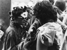 Verkleidete Frau mit Wäscheklammern im Haar, Sonnenbrille und Papiermaske im Gesicht in Menschenmenge; wahrscheinlich Hetero Garanti(e) 04.08.1981