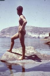 Junger Mann posiert nackt auf Stein am Meer, Rückenansicht, um 1945