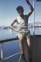 Junger Mann in schmuddeligen Shorts und Trägerleibchen sitzt an Reling auf einem Schiff, um 1950