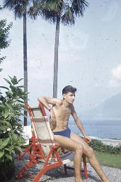 Junger Mann sitzt auf Armlehne eines Liegestuhls, am See, um 1950