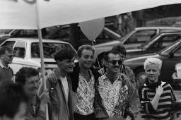 Drei sich umarmende Männer mit Hemd und Sweatshirt, weisser Ballon im Hintergrund; Demonstration 24.06.1989 zu 20 Jahre Stonewall während der Aktion "20 Tage lesbisch-schwule Kultur" 09.06 - 01.07.1989 in Zürich