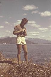 Bob Steffen in weissen Shorts, braunem Pulli steht am Ufer eines Sees und betrachtet etwas in seinen Händen, um 1950