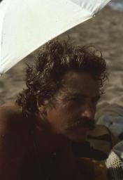 Porträt von Bob Steffen mit graumeliertem Wuschelhaar, unter Sonnenschirm am Strand, 1975