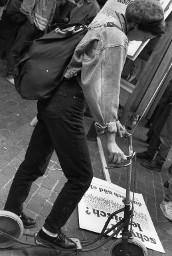 Frau mit kurzen Haaren und Hut auf einem Trettroller, studiert ein Plakat; Demonstration 24.06.1989 zu 20 Jahre Stonewall während der Aktion "20 Tage lesbisch-schwule Kultur" 09.06 - 01.07.1989 in Zürich