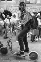 Frau mit kurzen Haaren und Hut auf einem Trettroller, eine Grimasse ziehend; Demonstration 24.06.1989 zu 20 Jahre Stonewall während der Aktion "20 Tage lesbisch-schwule Kultur" 09.06 - 01.07.1989 in Zürich