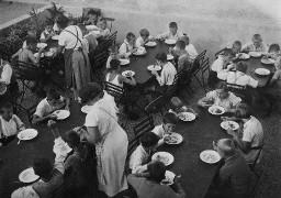 ...dann wird gefuttert - Kinder im Freien essen am Tisch und zwei Frauen servieren die Speisen