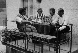 Vier Erwachsenen sitzen auf dem Balkon - Eine Frau strickend