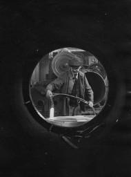 Arbeiter mit Schiebermütze beim Schweissen (?) in einer Werkhalle - Aufnahme durch ein Rohr, um 1940