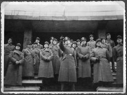 Album Alfred Brauchli, Teil 3/3, Ärzte- und Pflegermission des Schweizerischen Roten Kreuzes an der Ostfront, Winter 1942/1943: Gruppenfoto mit Leuten in Mäntel (vermutlich der Schweizer Armee) und mit Schweizerkreuz gekennzeichneten Feldmützen neben Männern in Uniform der Wehrmacht des Deutschen Reiches, "Ankunft in Berlin"