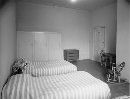Doppelzimmer mit kleinem Tisch, zwei Stühlen, Kommode und Schrank, um 1950