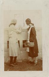 Zwei Frauen beim lesen einer Fassadenbeschriftung "Schweizerischer Nationalverein der Freundinnen junger Mäddchen Sektion Graubünden", um 1920