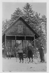 "Wochenendhäuschen des Mädchenklubs Fides Zürich", drei Frauen auf Skiern vor einem Haus, im Hintergrund auf der Veranda eine Frau und zwei Kinder, um 1950