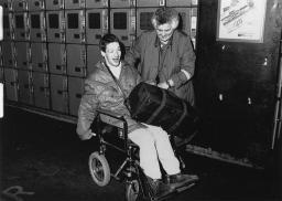 Ein Mann im Rollstuhl sitzend mit einer Mitarbeiterin der Freundinnen junger Mädchen in einem Bahnhof, 1989