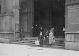 Drei Frauen aus einem Bahnhofsgebäude laufend, im Hintergrund mehrere Personen stehend, um 1910