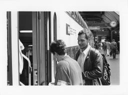 Eine Frau der SOS Bahnhofhilfe, einem Mann mit Beinträchtigung beim einsteigen in den Zug helfend, um 1990