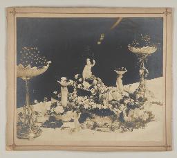 Wachsfiguren(?) auf einem Wagen, von Löwenfiguren(?) gezogen; flankiert von zwei Schalen Beeren, um 1910
