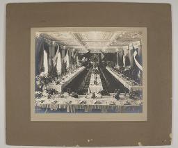 Reich gedecktes Bankett mit Blumen in einem Saal; prominent die Schweizer und Zürcher Fahne, darunter auch: Japan, Grossbritannien, Niederlande(?), Dänemark(?), Kanton Zürich, um 1910