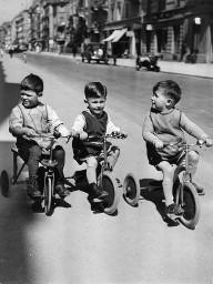 Drei Kinder fahren auf einer Strasse in der Stadt Dreirad