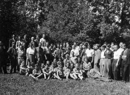 Gruppenfoto auf einer Wiese vor Bäumen mit ca. 50 Personen, vor den stehenden Erwachsenen sitzen die Kinder am Boden