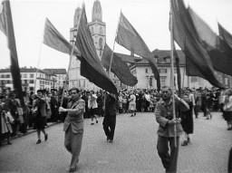 Eine Gruppe mit Fahnen marschiert durch die Altstadt von Zürich, im Hintergrund das Grossmünster