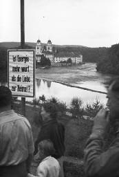Plakat "Ist Energie mehr wert als die Liebe zur Heimat?" am Wegrand, davor Demonstrationsteilnehmer auf dem Weg zur Klosterinsel Rheinau anlässlich der Kundgebung der Rheinaubewegung am 31.08.1952
